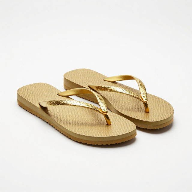 Fotografia de produto em estúdio com fundo branco infinito, um par de chinelos Havaianas Premium Feminino na cor dourada, destaque para os detalhes em metal e o brilho luxuoso. Sem texto na imagem, apenas visual.